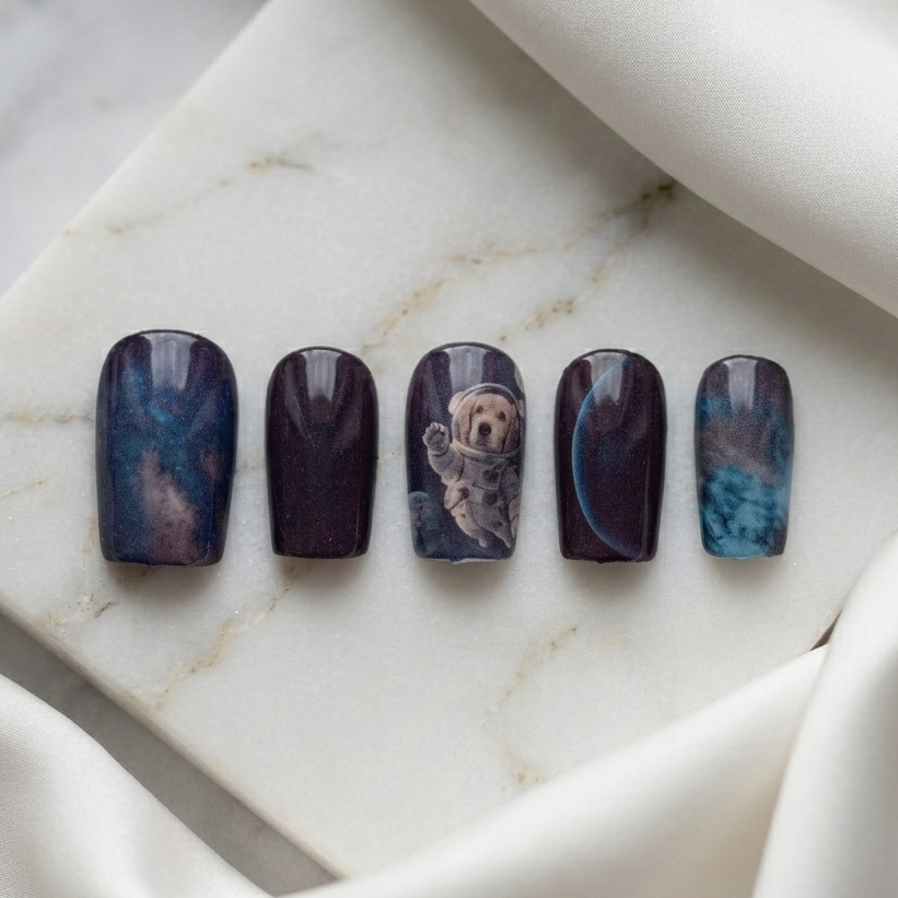 Press-on nails featuring a cute astronaut dog, galaxy patterns, and planets on a white stone base.