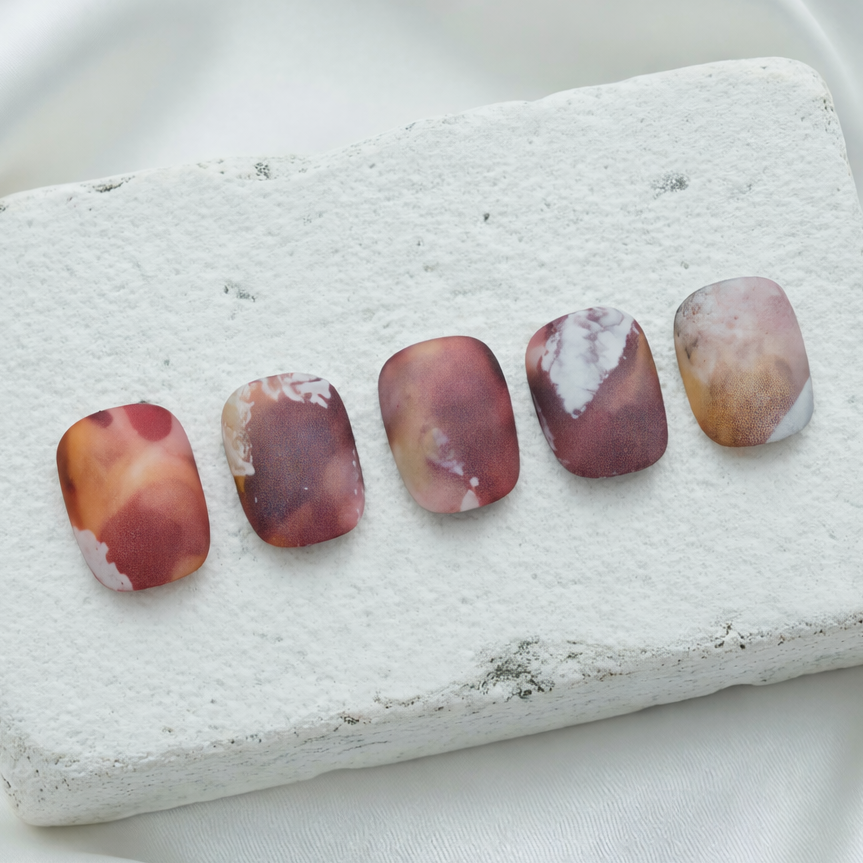 Earthy abstract press-on nails in matte brown and orange tones.