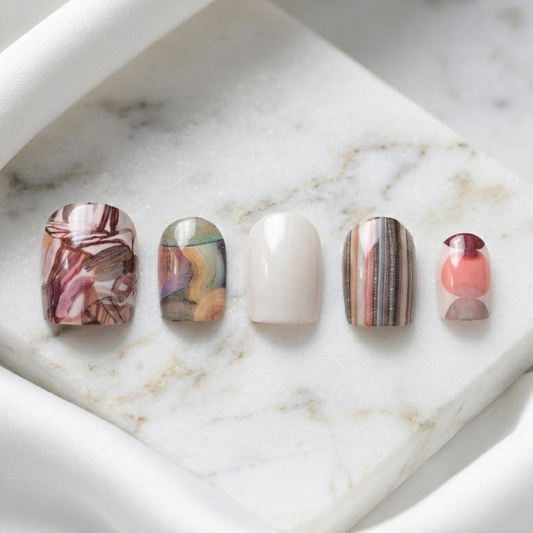 A selection of press-on nails with modern geometric designs, vertical stripes, and abstract shapes in neutral earth tones.
